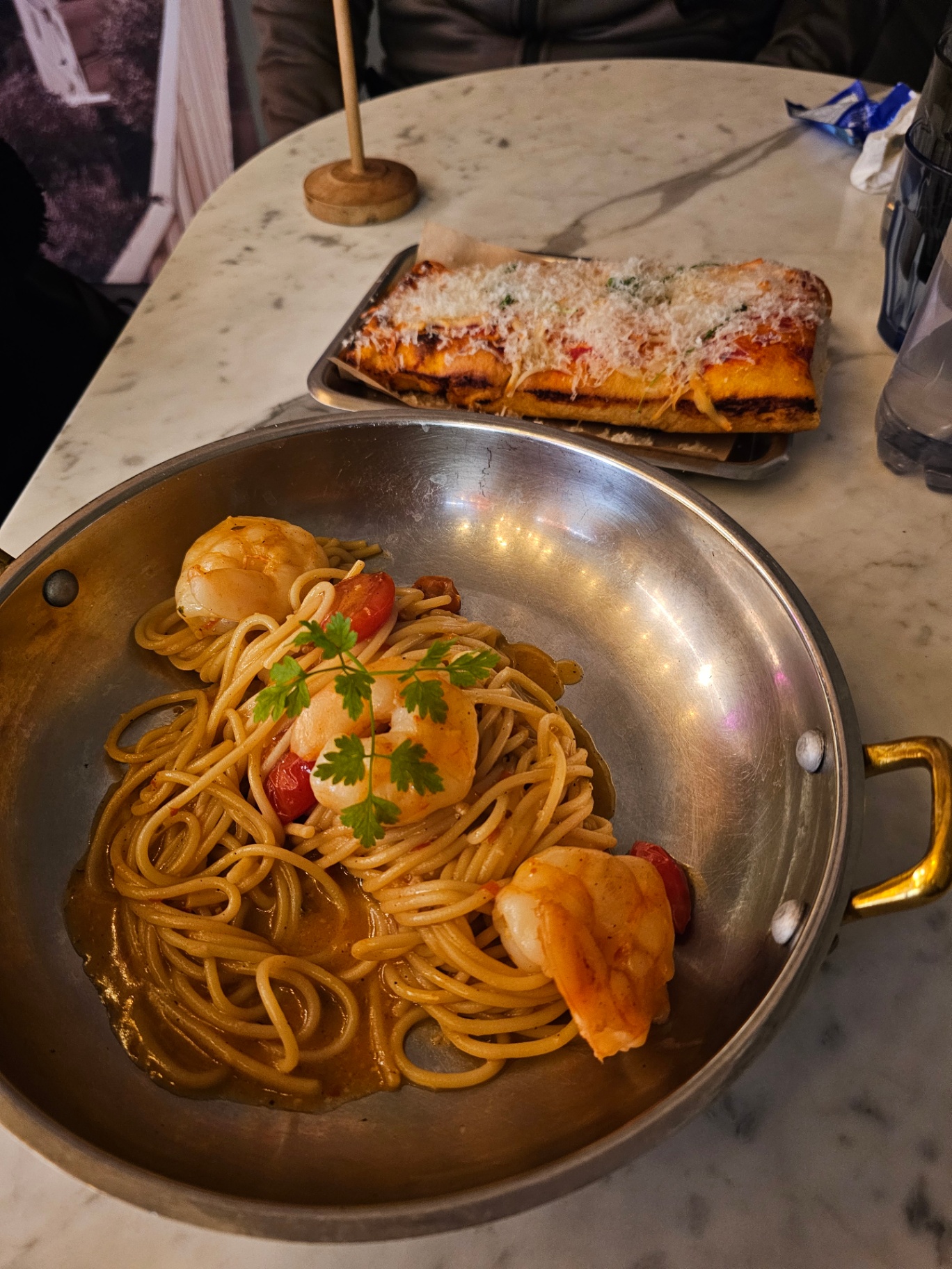 Shrimp spaghetti in a pan with pizza behind