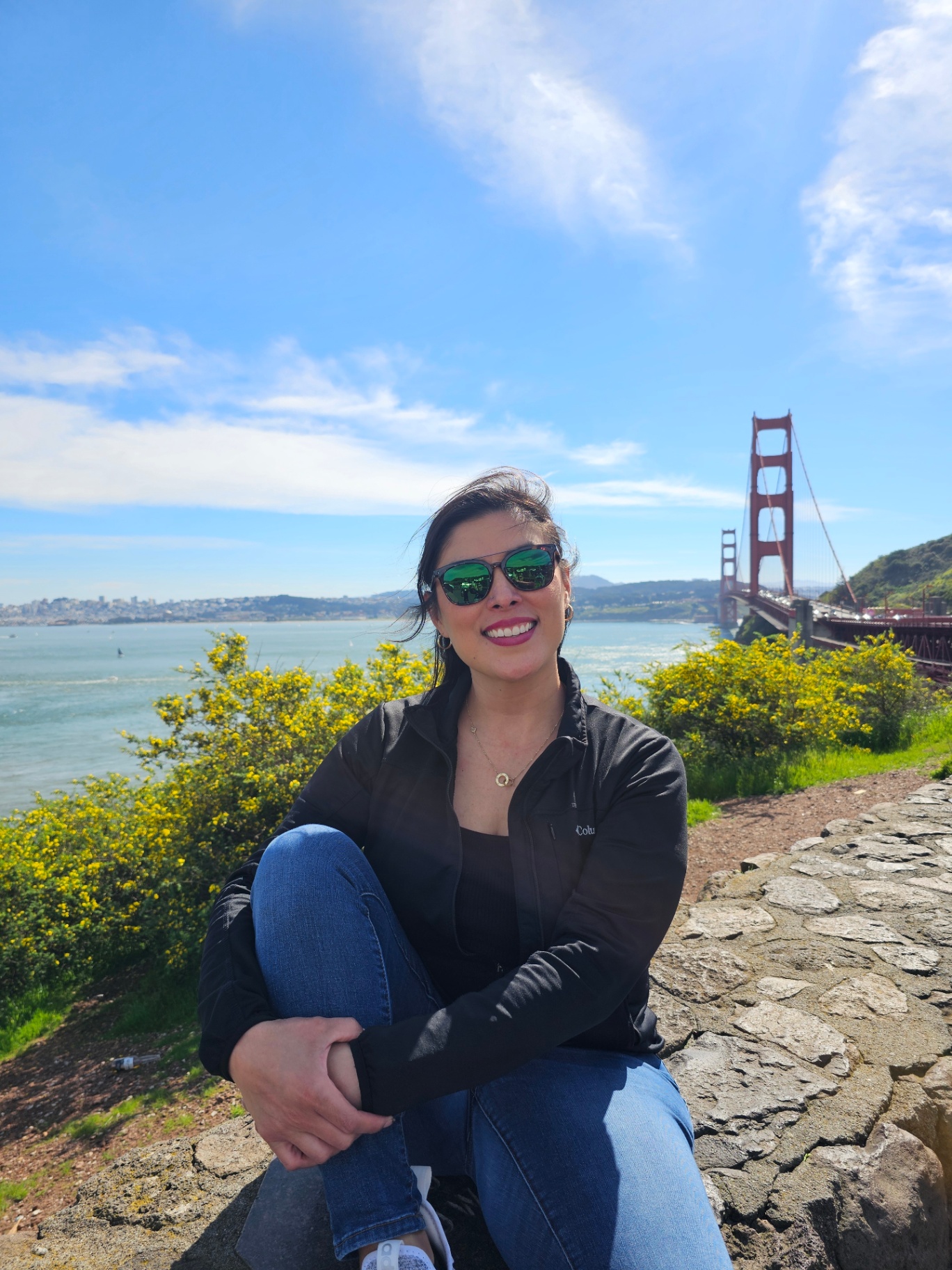 Woman sitting on a stone wall with the Golden Gate Bridge behind her