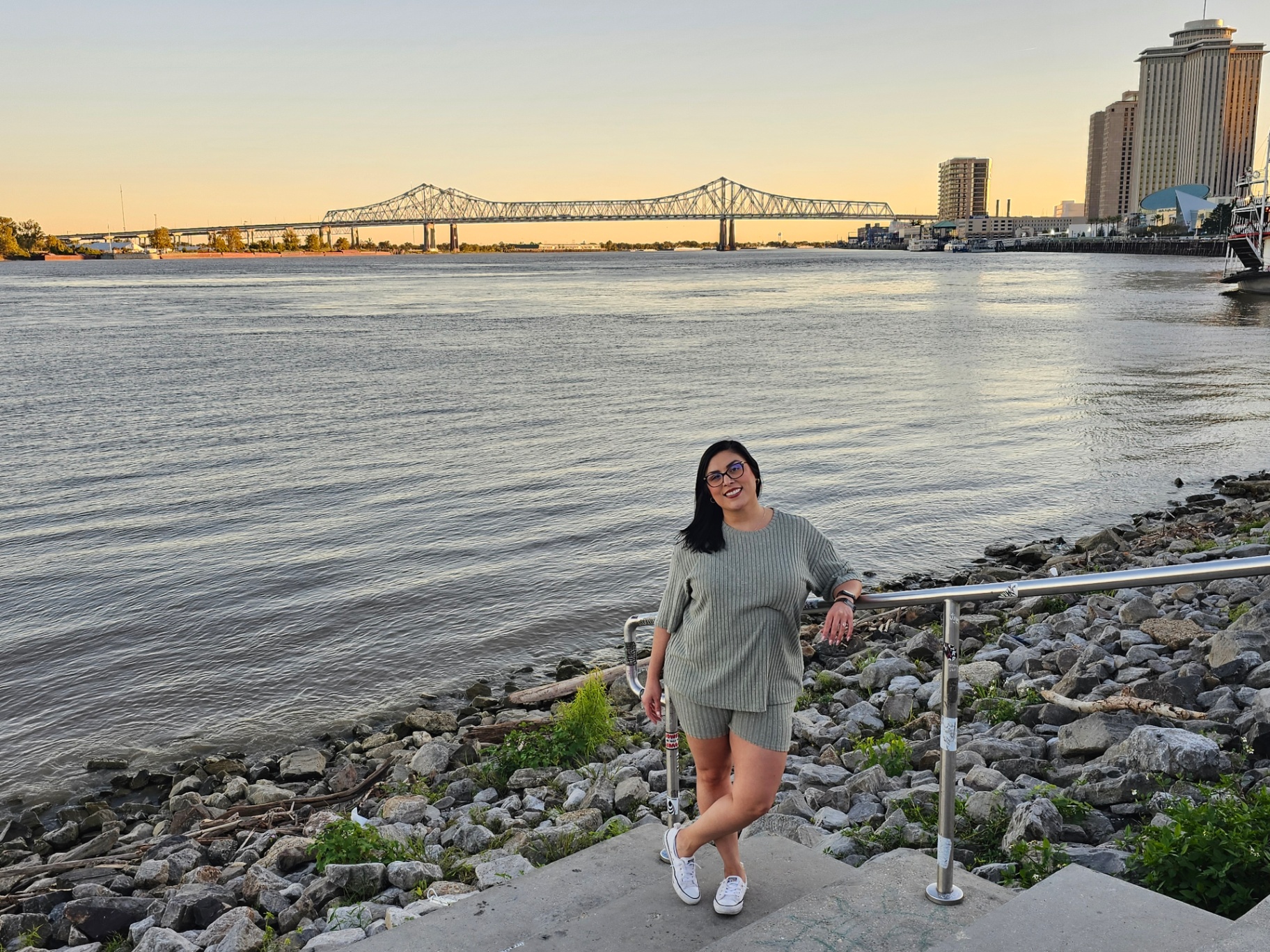 Woman by the Mississippi River at sunset with the Crescent City Connection bridge
