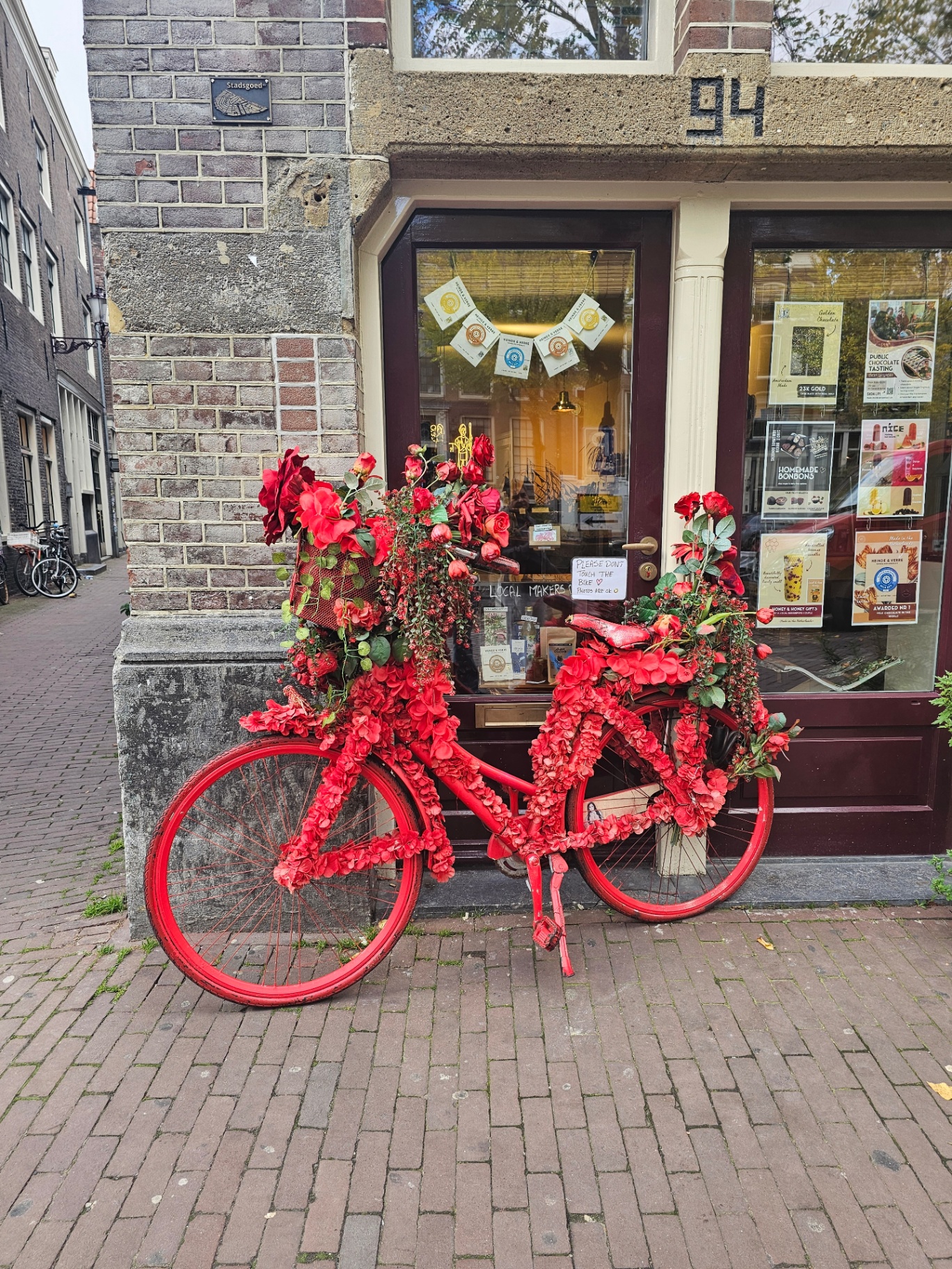 Red bicycle covered in red flowers outside an Amsterdam shop