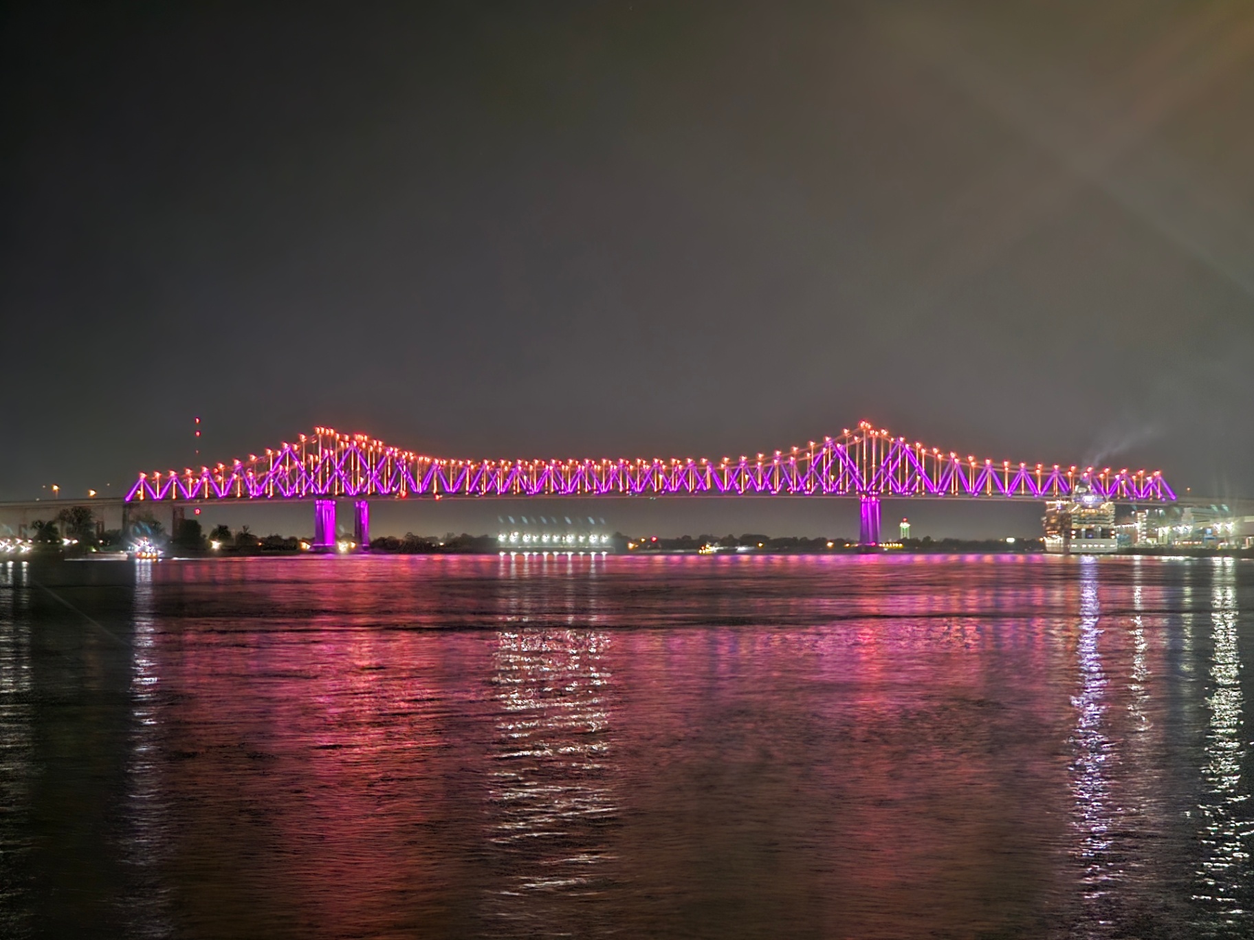 New Orleans bridge lit pink and purple over the river at night