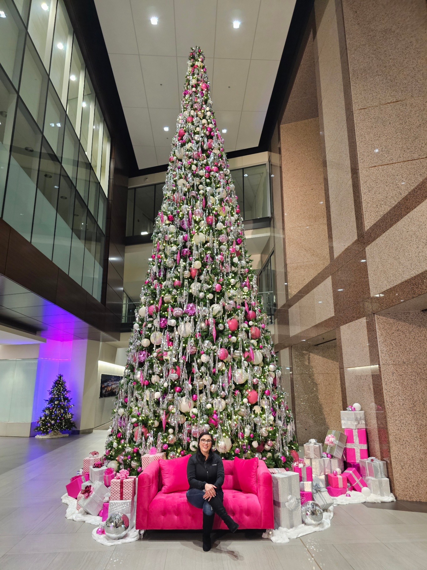 Woman on a pink sofa beneath a towering pink and silver Christmas tree